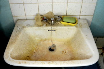 Messy bathroom sink, with dirty tap, soap and wall.