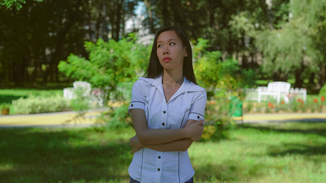 Sad asian woman in the park. Beautiful female stands on the street in summer season wearing in white shirt takes thought or sadden about something. Young businesswoman with long black hair wearing in
