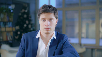 Portrait caucasian fashionable businessman looking at the camera sitting in the office. Adult male wearing in casual blue jacket.