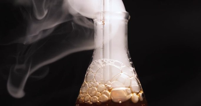 Flask with dark reagent and steam in chemical lab. Close-up view of flask with blue reagent and steam in chemical lab.