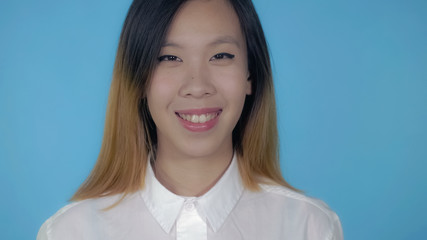 close up portrait young asian woman laughing on blue background in studio. attractive millennial girl looking at the camera