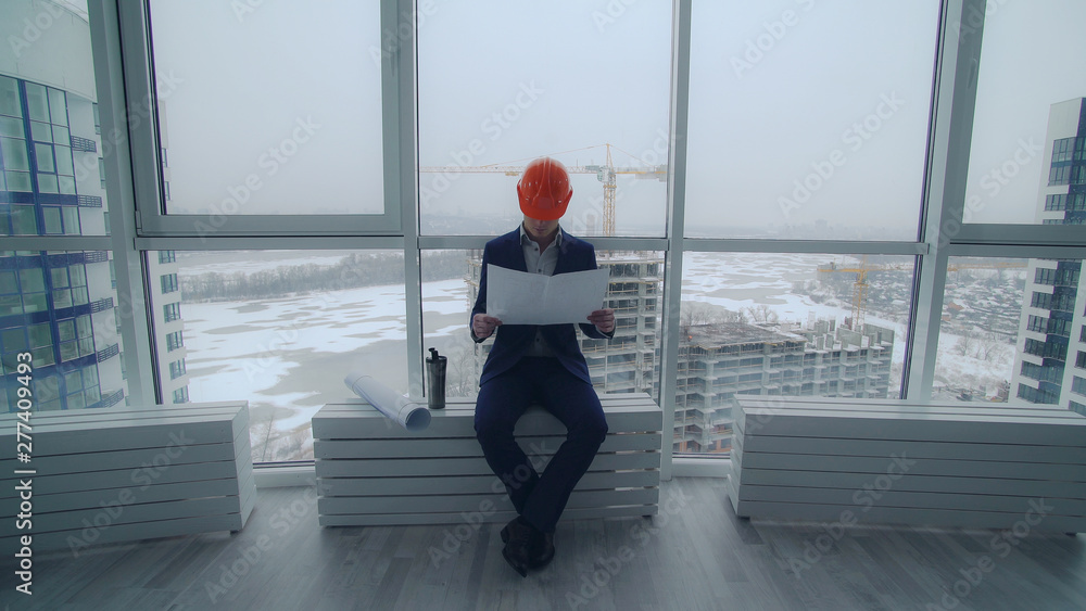 Aufkleber worker holding blueprint with floor map. architect wearing elegant suit and helmet sitting at constr