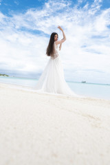 Fototapeta na wymiar A young bride in a white dress is standing on a snow-white beach.