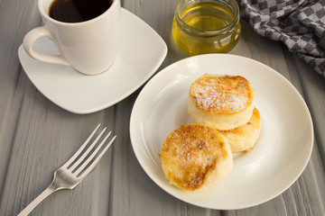 Breakfast: cheese pancakes, coffee  and honey  on the grey wooden background
