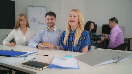 Obraz premium Coworkers wish a happy birthday with cake and candle. Employees enjoy party singing song in meeting room. Young people in startup company wearing casual clothes with happy smile sitting at the desk.