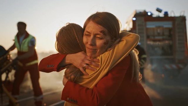Injured Mother and Young Daughter Reunite After Terrible Car Crash Traffic Accident, They Hug Happily. In the Background Through Smoke and Fire, Courageous Paramedics and Firefighters Save Lives