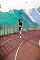 Sport. Athletic young brunette woman in pink sneakers, leggings and top run on running track stadium at sunset. her hair is developing. Concept run. concept of a healthy lifestyle.