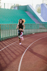 Sport. Athletic young brunette woman in pink sneakers, leggings and top run on running track stadium at sunset. her hair is developing. Concept run. concept of a healthy lifestyle.