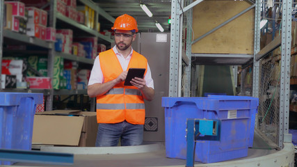 Warehouse worker standing near conveyor with parcels. Manager using digital tablet entering data....