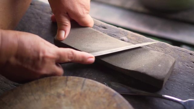 Old woman grind a knife with grinding stone for cooking. Traditional way.