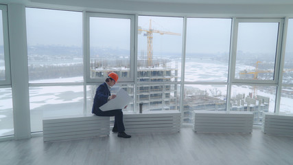 happy building engineer sitting in the modern office looking on the blue print documents with architectural plan. handsome man wearing in elegant suit and hard hat. At the construction site workers