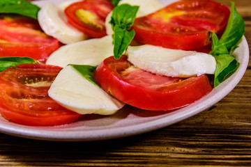 Plate with caprese salad (italian salad with cherry tomatoes, mozzarella cheese and basil leaves) on wooden table