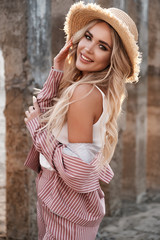 Portrait of a pretty, beautiful and romantic smiling young woman with long loose blonde hair in a straw hat. Countryside landscape, stones at the background. Summertime, summer outdoor photoshoot - 277411438