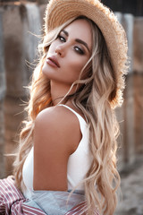Natural lifestyle portrait of a beautiful sexy young woman with long loose blonde hair in a straw hat. Countryside landscape at the background. Summertime, summer outdoor photoshoot - 277411613
