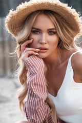 Natural lifestyle portrait of a beautiful gorgeous young woman with long loose blonde hair in a straw hat. Countryside landscape at the background. Summertime, summer outside photoshoot - 277411663