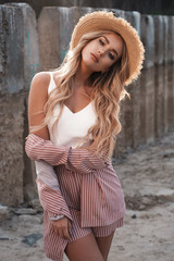 Portrait of a beautiful, romantic and stylish female model with long loose blonde hair in a straw hat. Countryside landscape, nature, stones and the sand at the background. Summertime, summer outdoor  - 277411690