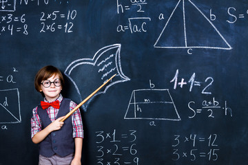 Intelligent smart schoolboy with eye glasses and wooden teacher pointer staying opposite school chalkboard during elementary mathematic lesson at school. Back to school, ready to study concept