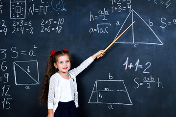 Intelligent smart schoolgirl girl with wooden teacher pointer staying opposite school chalkboard during elementary mathematic lesson at school. Back to school, ready to study concept