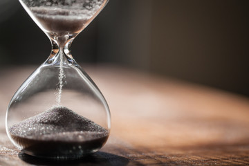 Sand running through the bulbs of an hourglass measuring the passing time in a countdown to a deadline with copy space.