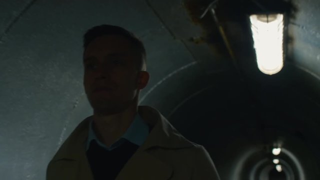 Tilt down shot of man in coat with roll plan, helmet and case in his arm going through the tunnel