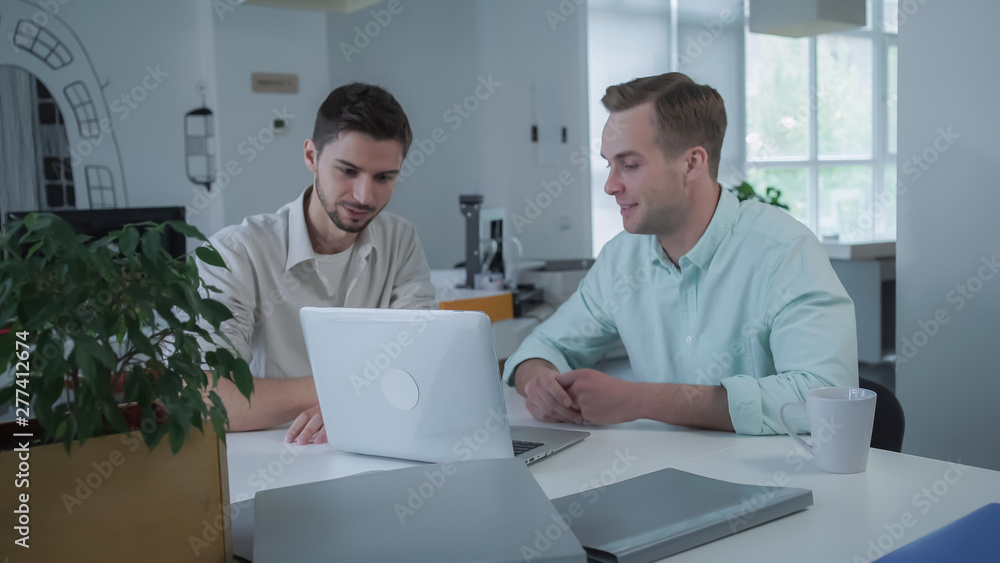 Aufkleber Coworkers designer debate new project. Man gesticulating and smiling while talking. Males working at the office with big windows.