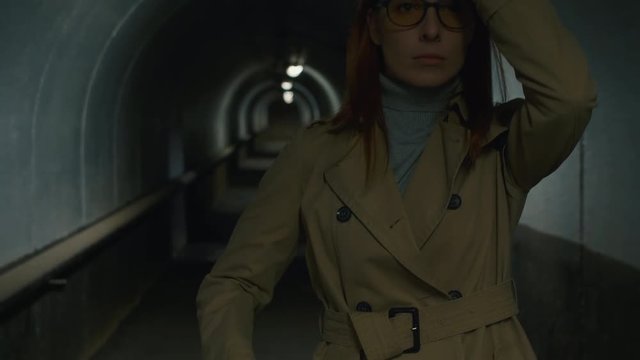 Up-section shot of businesswoman in glasses going through the tunnel with site plan and helmet under her arm, taking helmet and putting it on head