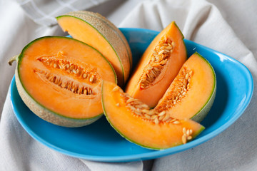Ripe and fresh cantaloupe melon. Bright orange fruit on a blue ceramic plate. Perfect food for hot summer party, delicious dessert. Cut in pieces, ready for eating, served cold