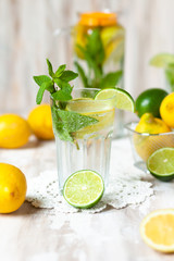 Summer composition with refreshing healthy alcohol free home made lemonade with pepper mint, limes and lemons. White lace napkin as decor, wooden background. Vacation mood, enjoying summertime