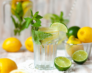 Summer composition with refreshing healthy alcohol free home made lemonade with pepper mint, limes and lemons. White lace napkin as decor, wooden background. Vacation mood, enjoying summertime