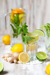 Summer composition with refreshing healthy alcohol free home made lemonade with pepper mint, limes and lemons. White lace napkin as decor, wooden background. Vacation mood, enjoying summertime