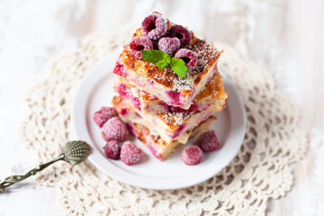 Delicious homemade cheesecake with raspberry, cut in rectangular pieces and put in stack. White plate, vintage knitted napkin, old spoon. Decorated with frozen berries and mint