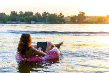 Young woman with laptop in the ring in the water during sunset, copy-space.