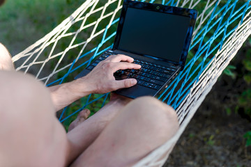 Freelancer working on a laptop lying in a hammock.