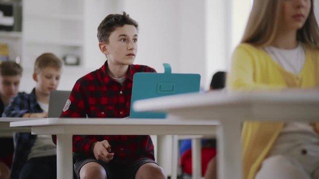 Young Students Passing Tests In A Computer Science Class. Focus On A Silly Boy Trying To Cheat With Handmade Crib During A Lesson.