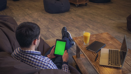 The man sits back in the hands holding the tablet, welcome companion, a green screen.
