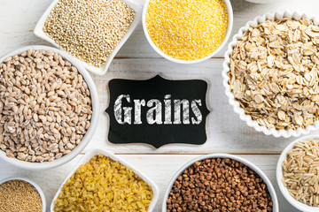 Selection of whole grains in white bowls - rice, oats, buckwheat, bulgur, porridge, barley, quinoa, amaranth, on white wood background
