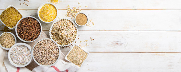 Selection of whole grains in white bowls - rice, oats, buckwheat, bulgur, porridge, barley, quinoa,...