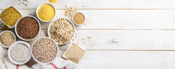 Tuinposter Selection of whole grains in white bowls - rice, oats, buckwheat, bulgur, porridge, barley, quinoa, amaranth, on white wood background © anaumenko