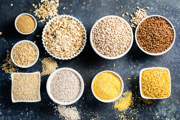Selection of whole grains in white bowls - rice, oats, buckwheat, bulgur, porridge, barley, quinoa, amaranth on dark background