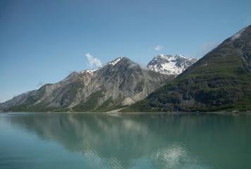 Fototapeta na wymiar Blue sky, dark grey mountains, and teal ocean water meet in Alaska's Glacier National Park