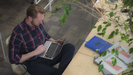 Bearded man drinking coffee and surf the Internet while relaxing on a chair. Static video