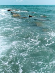 Naklejka premium abstract background of bright turquoise sea water, under the water a huge concrete stones as the breakers, the white foam of the surf, the sunlight sparkle on the ocean waves, a strip of azure sky