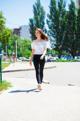 Young beautiful brunette woman in jeans and white blouse walking in summer street