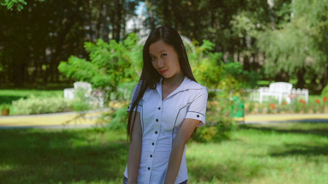 Young woman flirtatiously smile at the camera. Asian student standing in front of green tree. Embarrassed attractive girl smiling.Businesswoman wearing in formal shirt with short sleeves stands in the