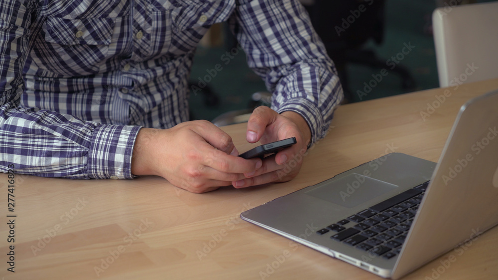 Poster busineman's hands texting message on smartphone. guy sitting at the wooden desk with computer in the