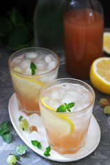 Gooseberry lemonade with mint and ice, a bottle of water and a bottle of gooseberry syrup on a concrete surface.