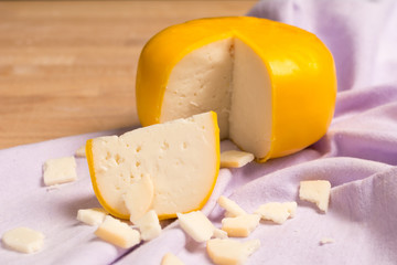 Yellow round cheese. Dutch goat cheese with pieces on wooden table.