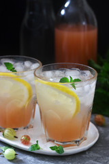 Gooseberry lemonade with mint and ice, a bottle of water and a bottle of gooseberry syrup on a concrete surface.