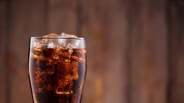 Full glass of cola with ice. Someone take it from the frame in slowmotion.