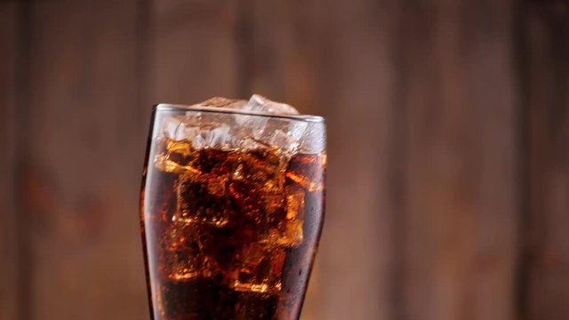 Full glass of cola with ice. Someone puts it in the frame in slow motion.